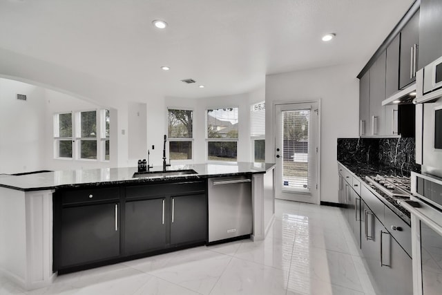 kitchen featuring stainless steel appliances, dark stone counters, sink, and decorative backsplash