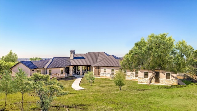 rear view of property featuring metal roof, stone siding, a yard, and stucco siding