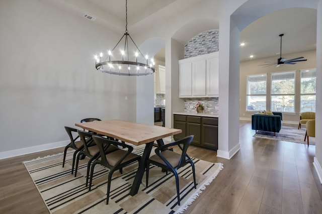 dining area featuring a high ceiling, light hardwood / wood-style floors, and ceiling fan with notable chandelier