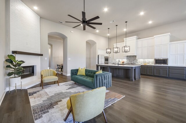 living room featuring dark wood-type flooring, sink, ceiling fan with notable chandelier, and a fireplace