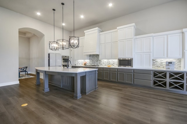 kitchen with stainless steel appliances, a kitchen island with sink, white cabinets, pendant lighting, and dark hardwood / wood-style flooring