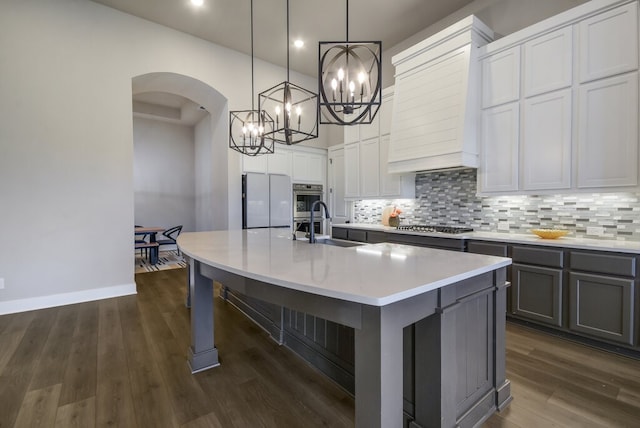 kitchen with stainless steel appliances, a center island with sink, dark hardwood / wood-style floors, decorative light fixtures, and gray cabinets