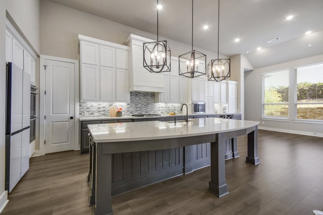 kitchen featuring an island with sink, white cabinets, decorative light fixtures, and dark hardwood / wood-style flooring