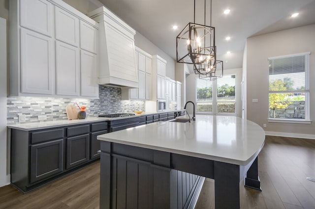 kitchen featuring a center island with sink, white cabinetry, decorative light fixtures, custom range hood, and dark hardwood / wood-style flooring