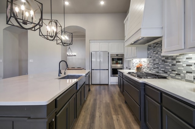 kitchen with stainless steel appliances, white cabinets, hanging light fixtures, a kitchen island with sink, and premium range hood