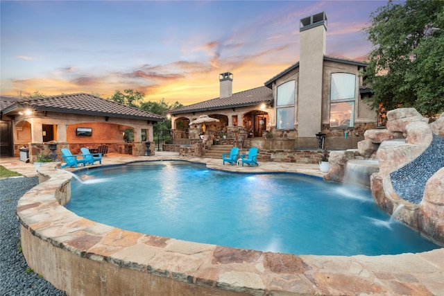 pool at dusk featuring a patio, a jacuzzi, and pool water feature