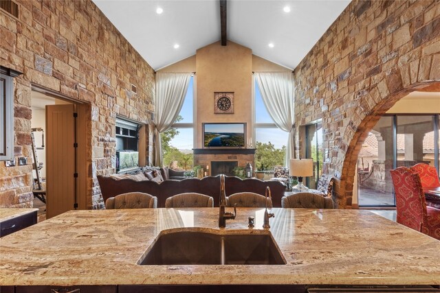 kitchen with light stone counters, sink, an outdoor stone fireplace, high vaulted ceiling, and beam ceiling