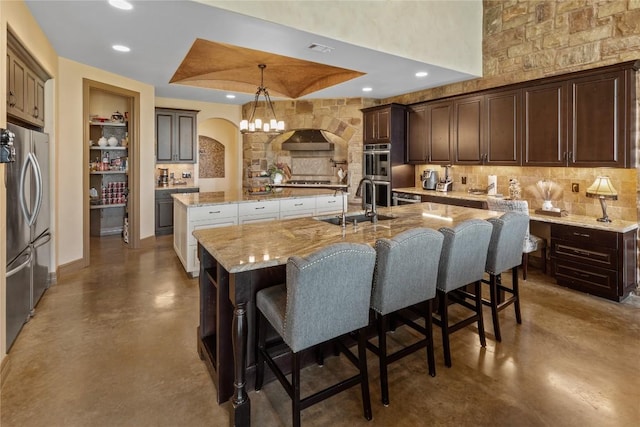 kitchen with arched walkways, a sink, a large island, appliances with stainless steel finishes, and finished concrete floors