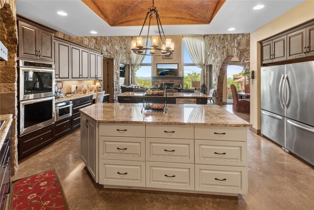 kitchen featuring dark brown cabinetry, stainless steel appliances, cream cabinets, a raised ceiling, and a kitchen island with sink