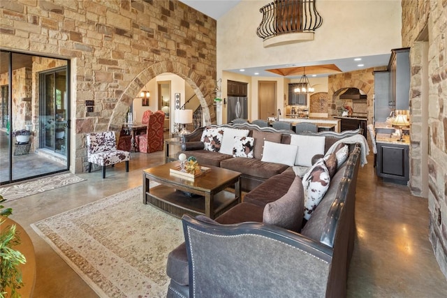 living room featuring arched walkways, a high ceiling, an inviting chandelier, and finished concrete floors