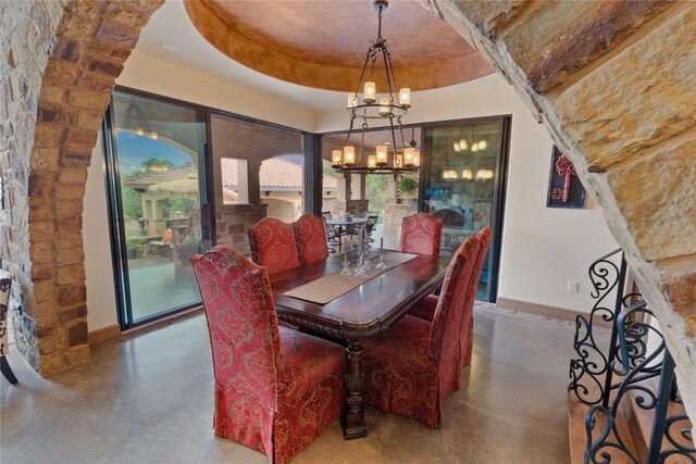 dining room with concrete flooring, a tray ceiling, and a notable chandelier