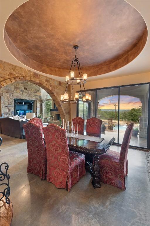 dining room featuring an inviting chandelier, arched walkways, a raised ceiling, and concrete flooring