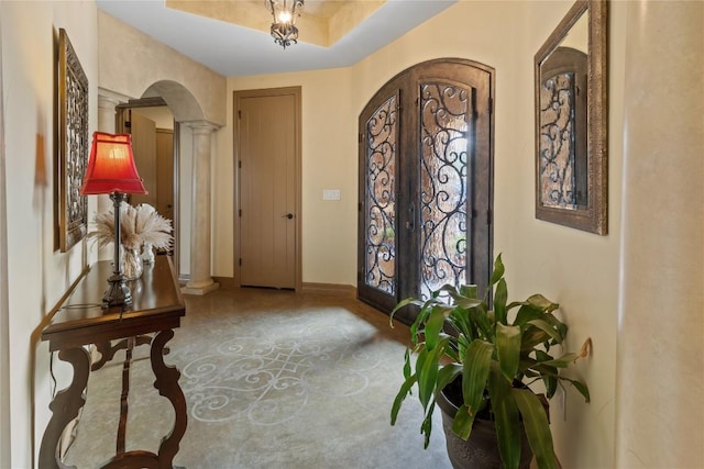 entrance foyer with arched walkways, french doors, decorative columns, a raised ceiling, and baseboards