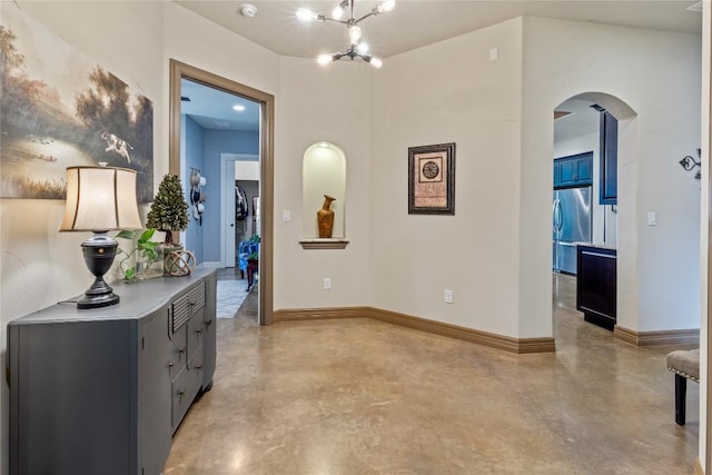 hallway featuring concrete flooring, an inviting chandelier, arched walkways, and baseboards