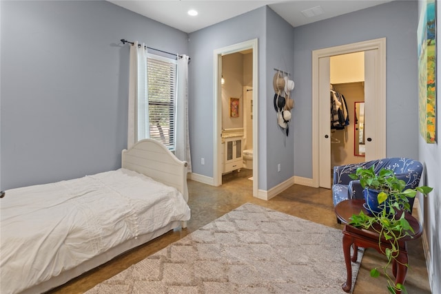 bedroom with a walk in closet, concrete floors, and ensuite bath