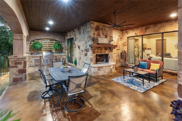 view of patio / terrace featuring exterior kitchen, outdoor dining space, an outdoor living space with a fireplace, and a ceiling fan