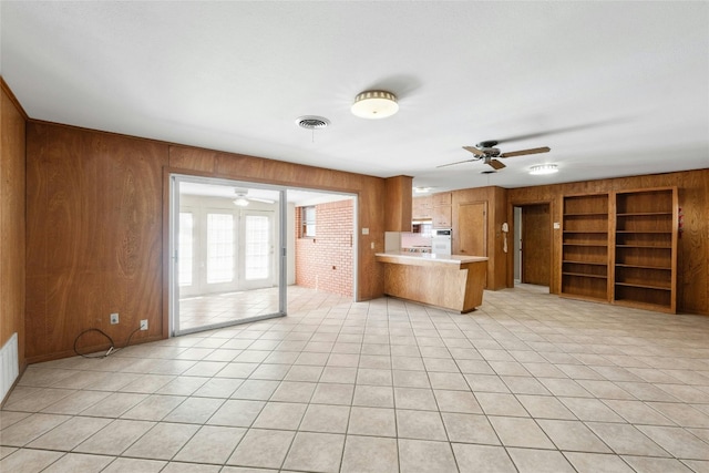 kitchen featuring built in features, light tile patterned flooring, wood walls, kitchen peninsula, and ceiling fan