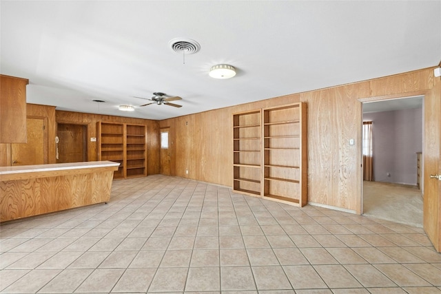 unfurnished living room with built in shelves, wooden walls, light tile patterned floors, and ceiling fan