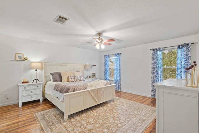 bedroom with ceiling fan, multiple windows, a textured ceiling, and wood-type flooring