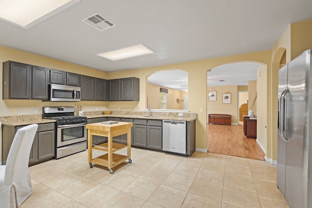 kitchen with light hardwood / wood-style floors, dark brown cabinetry, sink, light stone countertops, and appliances with stainless steel finishes