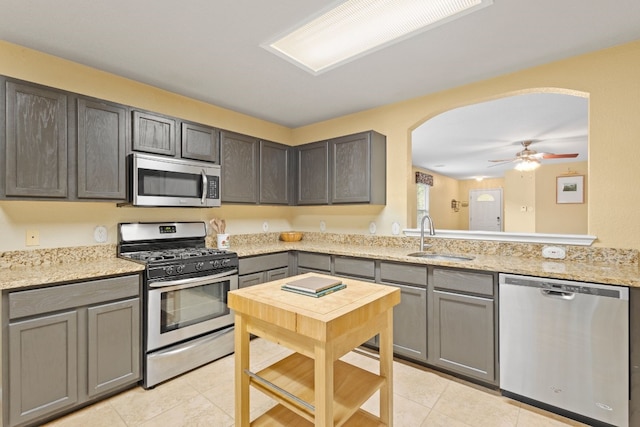 kitchen with stainless steel appliances, light tile patterned flooring, sink, light stone countertops, and ceiling fan