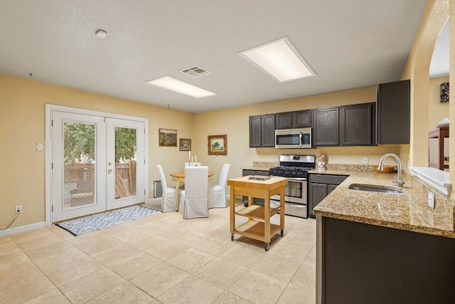 kitchen featuring sink, light stone counters, appliances with stainless steel finishes, dark brown cabinets, and french doors