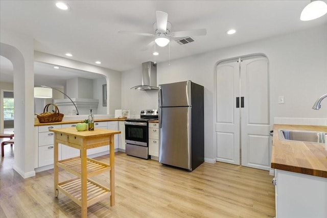 kitchen featuring appliances with stainless steel finishes, white cabinetry, sink, wooden counters, and wall chimney range hood