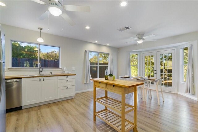 kitchen featuring sink, hanging light fixtures, white cabinets, stainless steel dishwasher, and light wood-type flooring