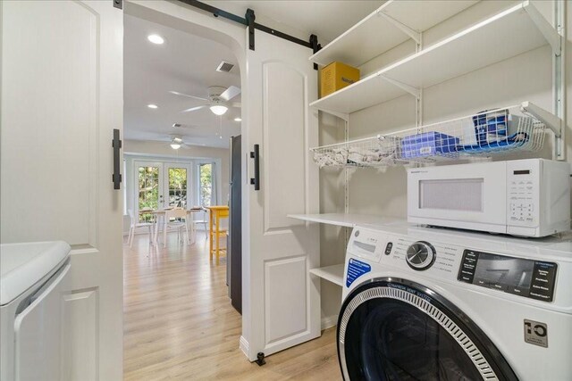 washroom featuring ceiling fan, a barn door, separate washer and dryer, and light wood-type flooring