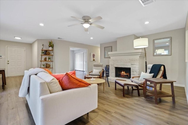 living room featuring a fireplace, ceiling fan, and light wood-type flooring