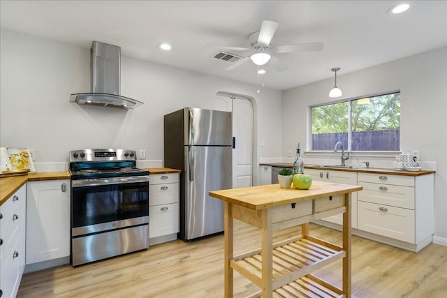 kitchen with pendant lighting, butcher block countertops, wall chimney range hood, appliances with stainless steel finishes, and white cabinets