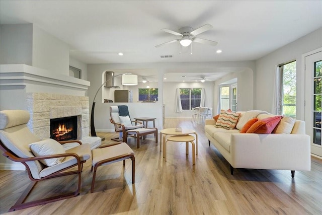 living room featuring ceiling fan, a stone fireplace, and light hardwood / wood-style floors