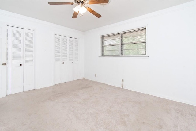 unfurnished bedroom with ceiling fan, carpet floors, ornamental molding, and multiple closets