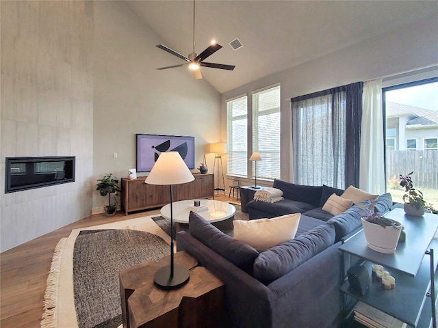 living room with high vaulted ceiling, a tiled fireplace, light hardwood / wood-style floors, and ceiling fan