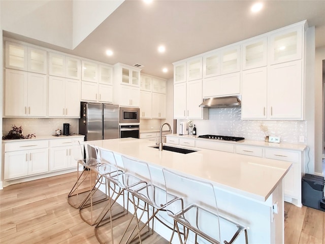 kitchen featuring stainless steel appliances, a kitchen bar, exhaust hood, sink, and a kitchen island with sink