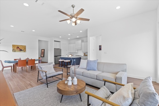 living room with light wood-type flooring, sink, and ceiling fan