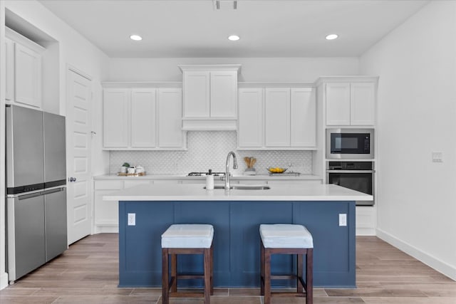 kitchen featuring white cabinetry, appliances with stainless steel finishes, an island with sink, and light wood-type flooring