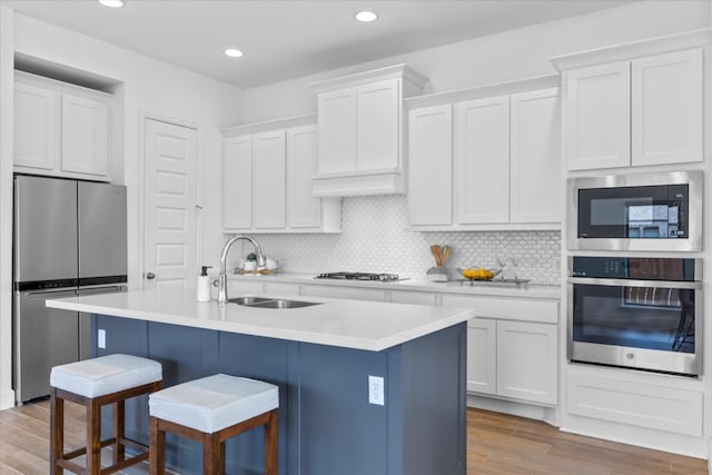 kitchen featuring light hardwood / wood-style floors, a center island with sink, white cabinetry, and appliances with stainless steel finishes