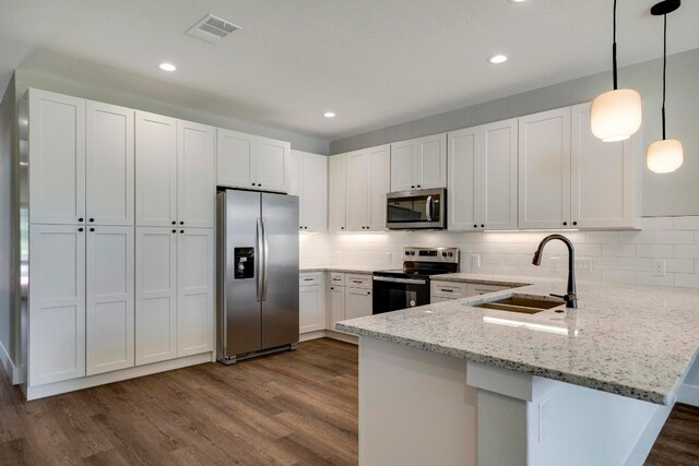 kitchen with sink, kitchen peninsula, appliances with stainless steel finishes, hanging light fixtures, and dark hardwood / wood-style flooring