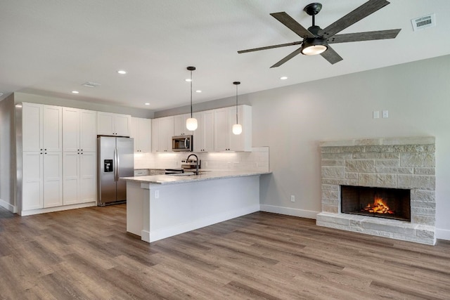 kitchen featuring light wood-type flooring, white cabinetry, appliances with stainless steel finishes, decorative light fixtures, and kitchen peninsula