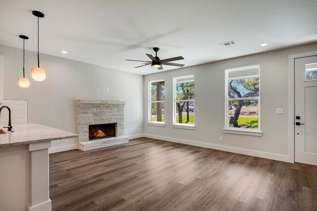 unfurnished living room with a stone fireplace, a textured ceiling, dark hardwood / wood-style floors, sink, and ceiling fan