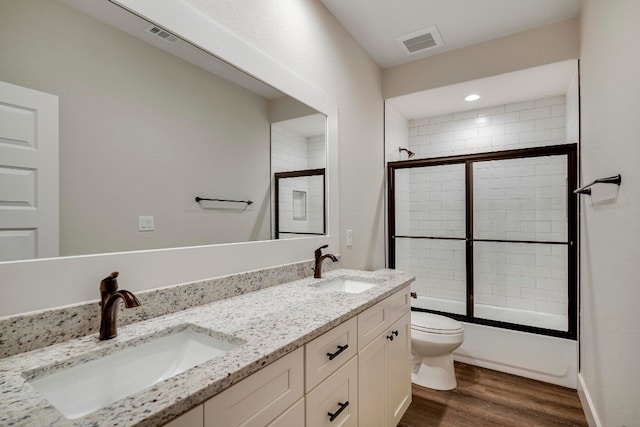 full bathroom featuring hardwood / wood-style floors, bath / shower combo with glass door, vanity, and toilet