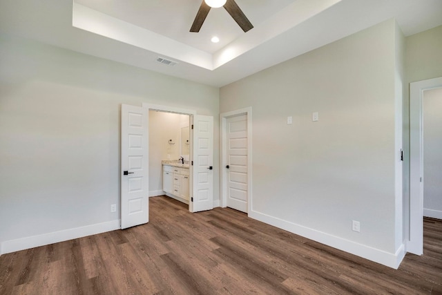 unfurnished bedroom featuring dark hardwood / wood-style flooring, sink, connected bathroom, ceiling fan, and a tray ceiling