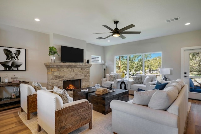 living room featuring ceiling fan, a stone fireplace, and light hardwood / wood-style flooring