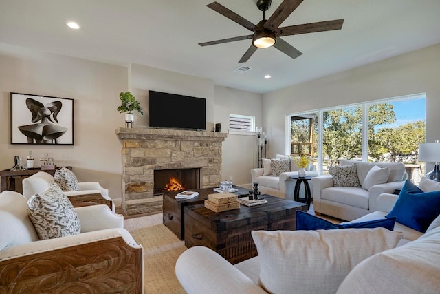 living room with a stone fireplace, light wood-type flooring, and ceiling fan