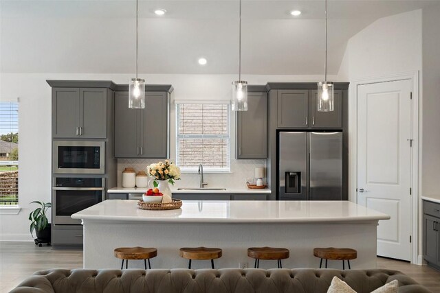 kitchen featuring gray cabinetry, tasteful backsplash, appliances with stainless steel finishes, hanging light fixtures, and sink