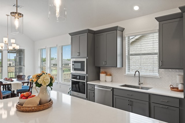 kitchen with stainless steel appliances, lofted ceiling, sink, gray cabinetry, and decorative light fixtures