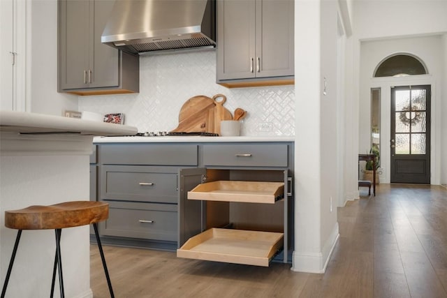 kitchen with gray cabinetry, gas stovetop, dark hardwood / wood-style floors, decorative backsplash, and wall chimney exhaust hood