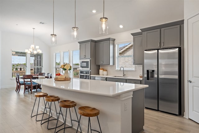 kitchen with sink, appliances with stainless steel finishes, a kitchen island, gray cabinets, and vaulted ceiling