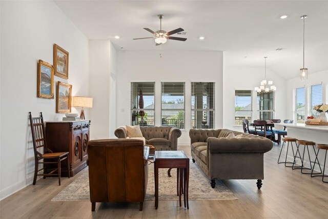 living room with ceiling fan with notable chandelier, plenty of natural light, light hardwood / wood-style floors, and vaulted ceiling